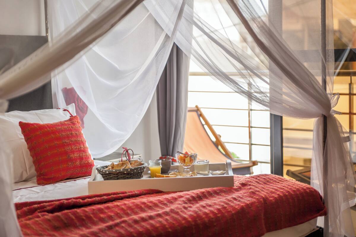 A bed with a red blanket, a red pillow, and a tray with breakfast items.
