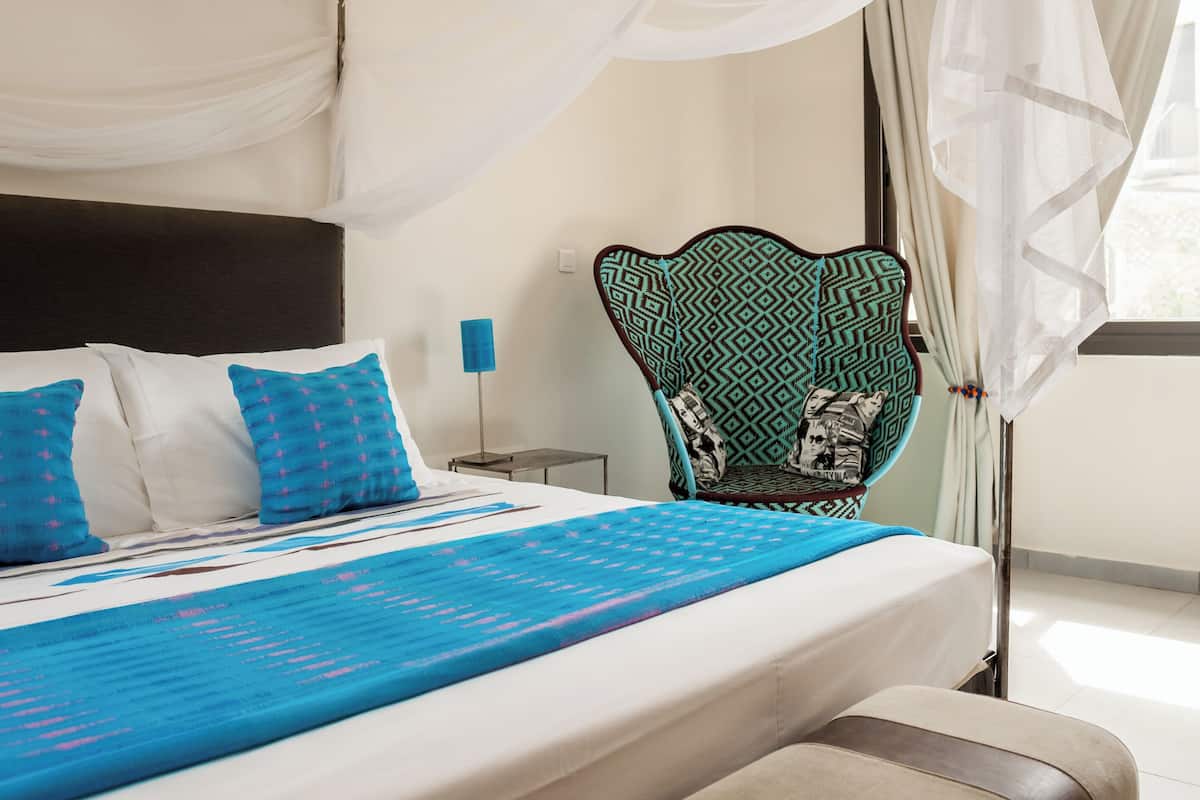 A bedroom with a bed, pillows, a nightstand, a lamp, and a chair.