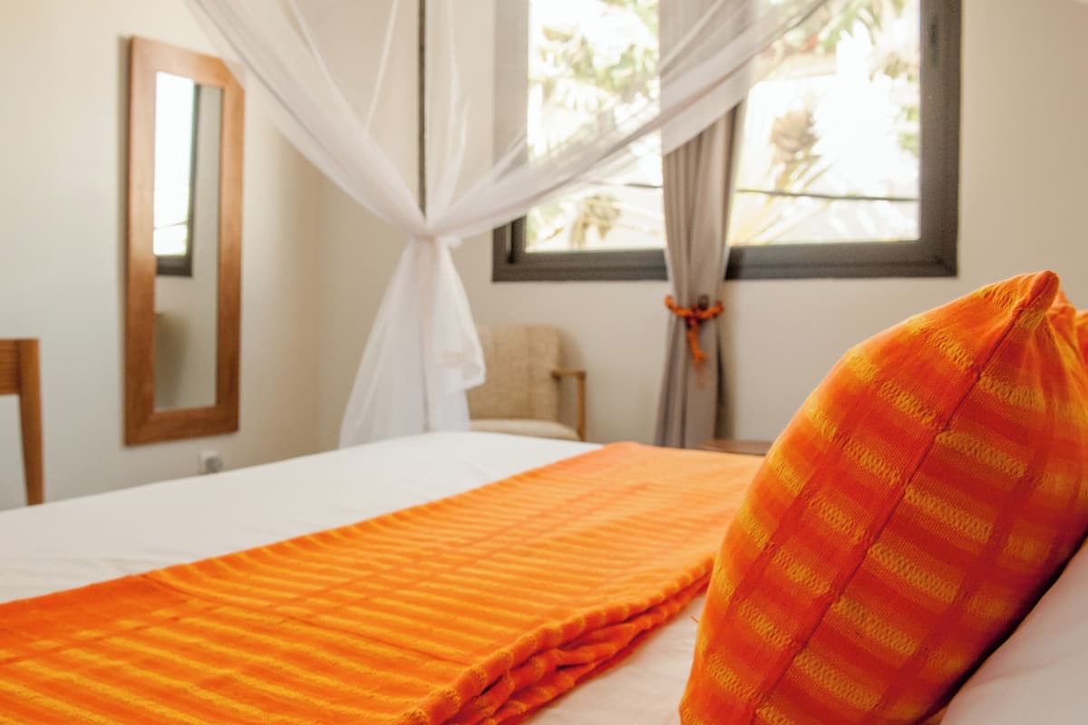 A hotel room with a bed, a window with curtains, a mirror, and a chair.
