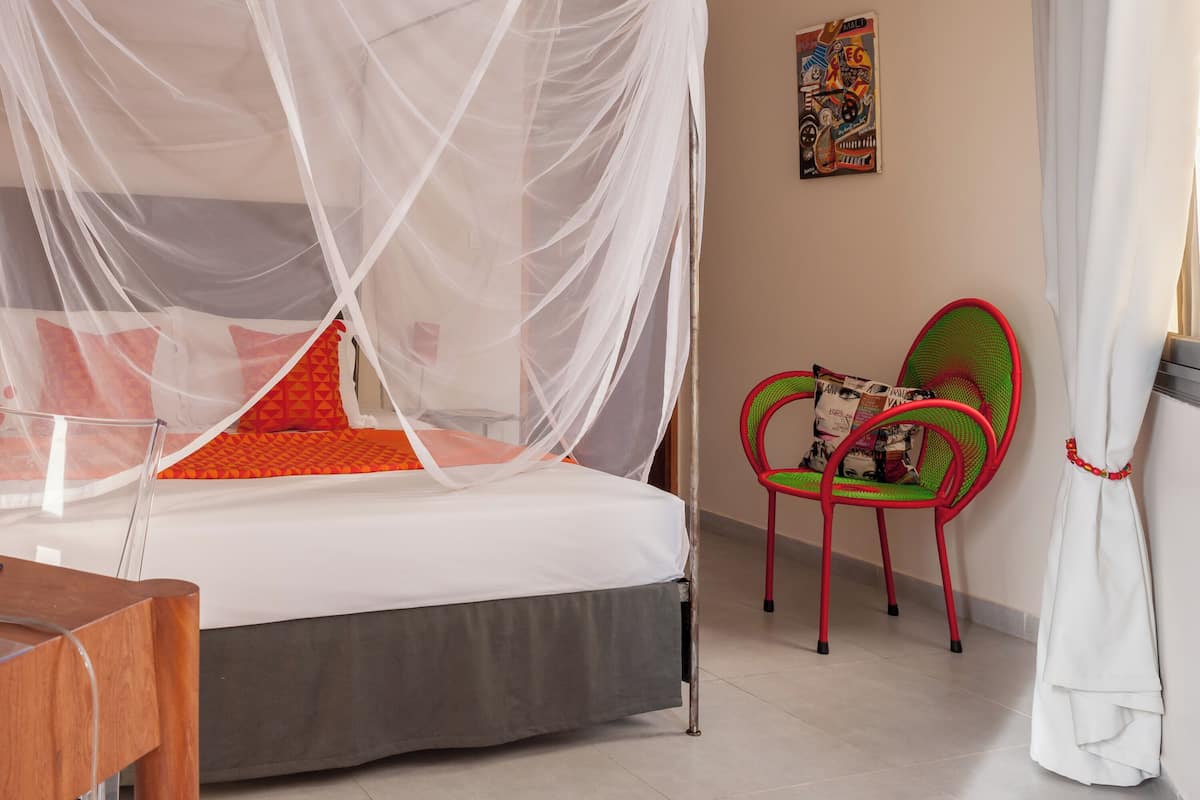 A bed with a white canopy, a red and green chair, and a painting on the wall.