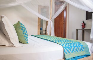 Cama com lençol branco, manta azul e verde estampada e um dossel branco.