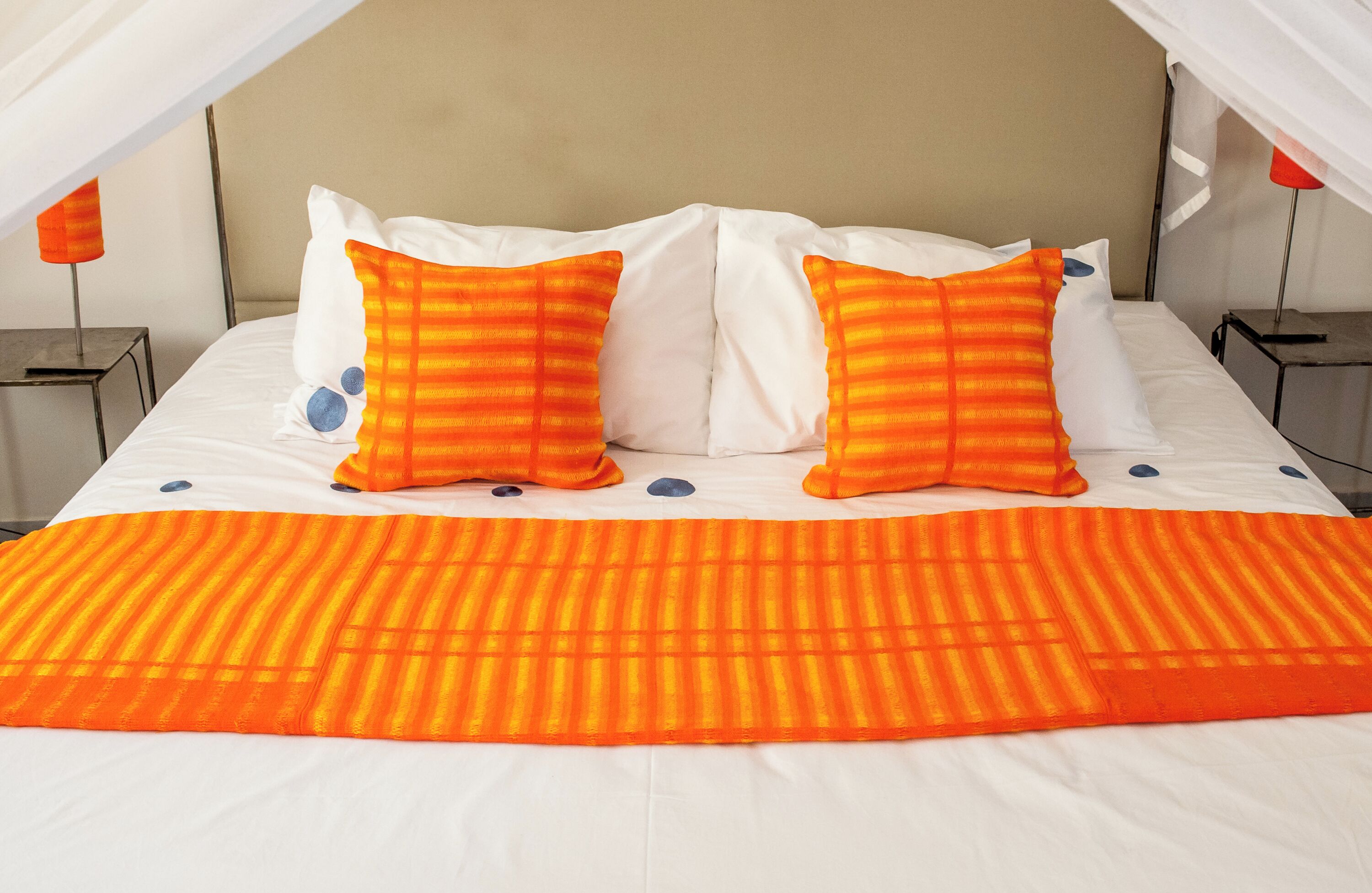Ein Bett mit weißer und orangefarbener Bettwäsche, zwei Nachttische und ein Baldachin.