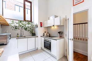 A compact kitchen with white cabinets, a built-in oven, a sink, and a window with a view of a brick building.