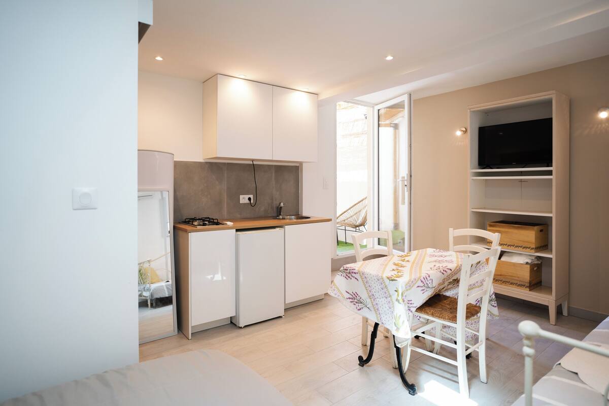 A compact kitchen with white cabinets, a small refrigerator, and a dining area with a table and chairs.