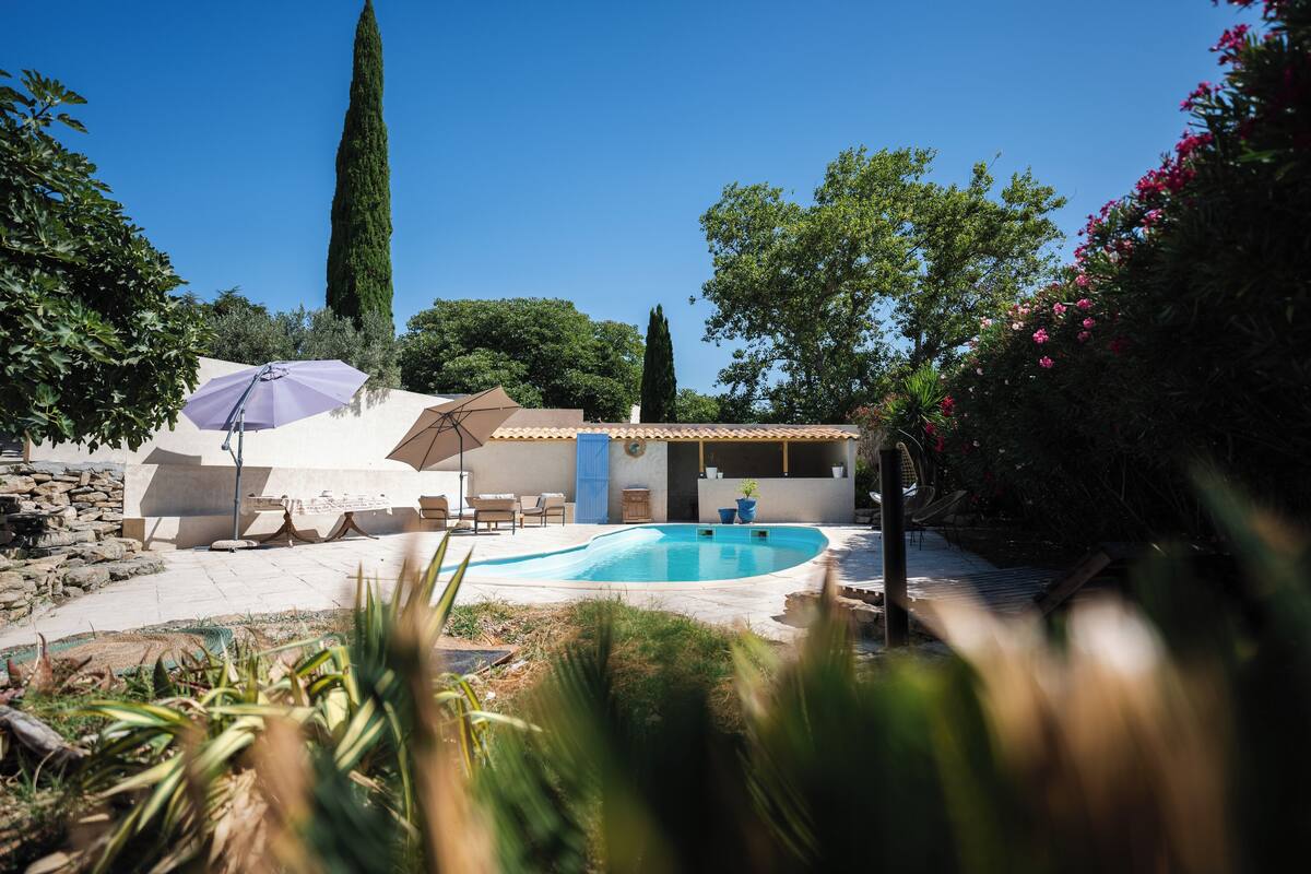 A modern outdoor pool area with a stone wall, lounge chairs, and a pergola with umbrellas.
