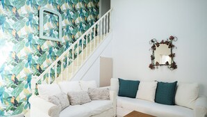 A living room with a white sofa, a wooden coffee table, a staircase with a white railing, and a wall with a mirror and a floral wallpaper. - La Bastide Bleue La Ciotat (La Ciotat)