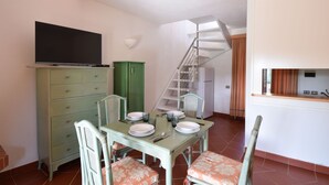 A dining area with a table set for four, a television on a cabinet, and a staircase leading to an upper level. - Casa Ortensia (Budoni)