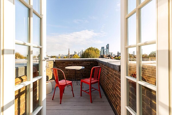 A rooftop terrace with two red chairs and a small table, overlooking a city skyline. - Charming Loft in Islington - Stunning View! (London)