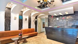 A hotel lobby with a reception desk, a sofa, a coffee table, and a chandelier.