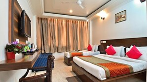 A hotel room with two beds, a desk with a chair, a TV, a window with curtains, and a ceiling fan.