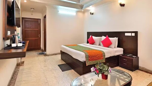 A hotel room with a bed, bedside table, and a glass coffee table with flowers.