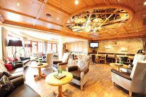 A spacious lobby with a wooden ceiling, comfortable seating areas, a television, and a stone accent wall. - Hotel Salnerhof Ischgl (Ischgl)
