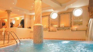 An indoor swimming pool with a central column, surrounded by walls with circular windows and mirrors. - Hotel Salnerhof Ischgl (Ischgl)