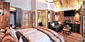 A modern hotel room with a large bed, a cozy seating area, a small table, and a TV mounted on the wall. - Hotel Salnerhof Ischgl (Ischgl)