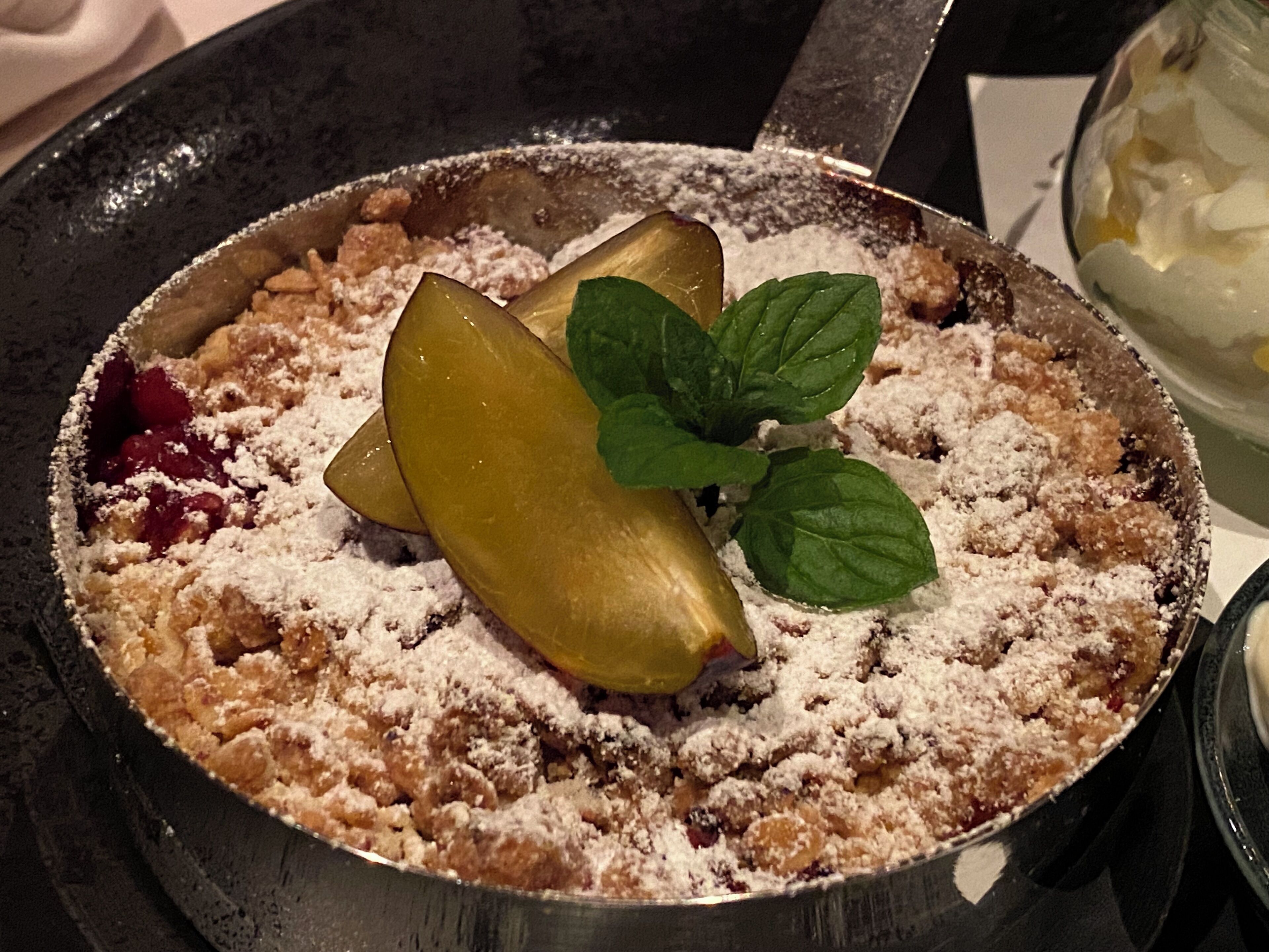 A dessert in a pan with a crumbled topping and a mint leaf garnish.