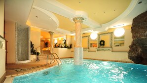 An indoor swimming pool with clear water, a central column, and a staircase leading to an upper level. - Hotel Salnerhof Ischgl (Ischgl)
