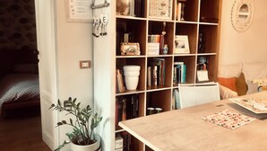 A cozy room with a wooden bookshelf filled with books and decorative items, a dining table with a placemat, and a potted plant.