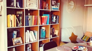 A cozy living room with a bookshelf filled with books, a white couch with cushions, and a coffee table with mugs.