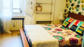 A bedroom with a bed, a white wardrobe, a window with curtains, and a wall with a circular pattern.