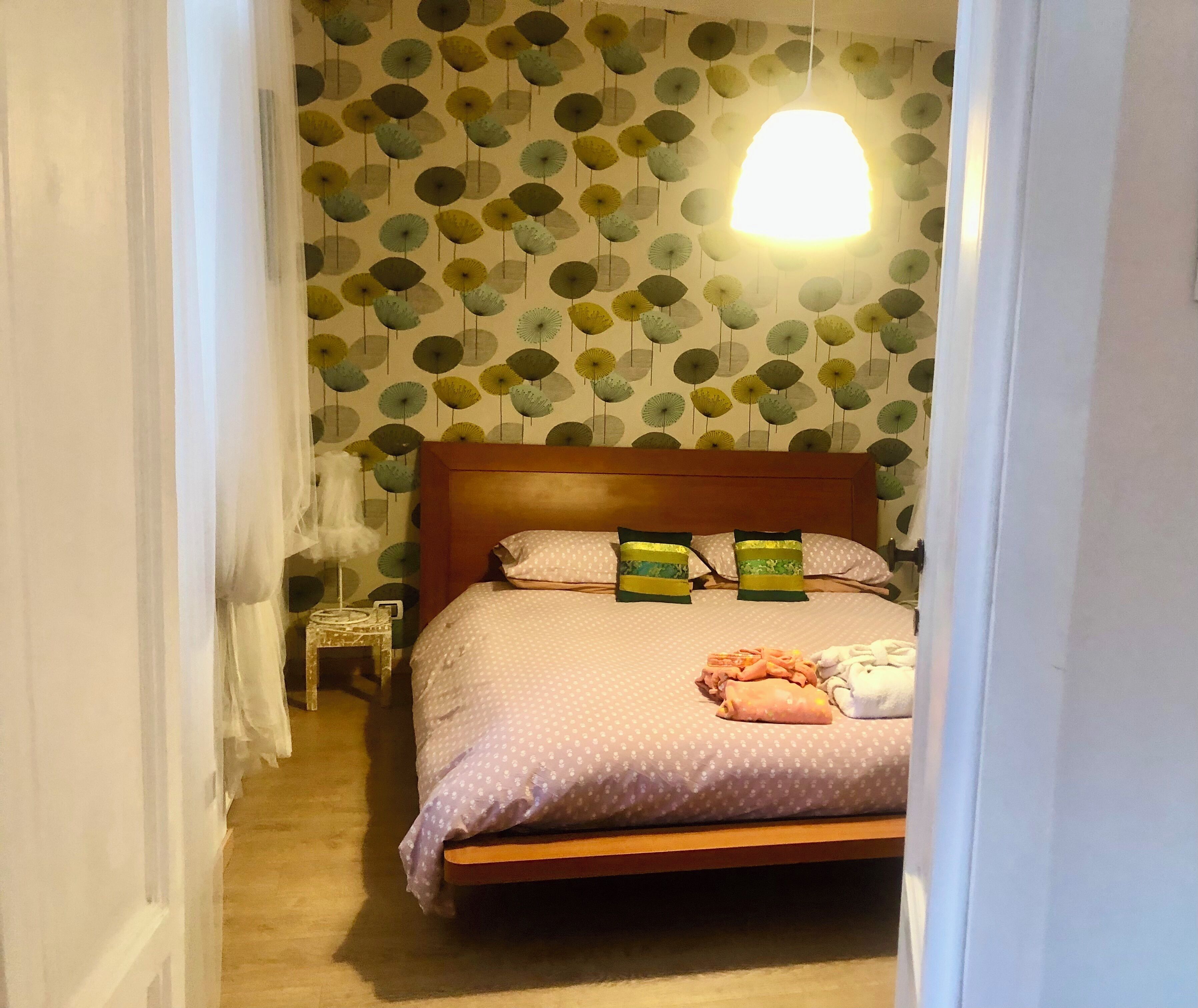 Een slaapkamer met een houten bed, behang met een patroon en een hanglamp.