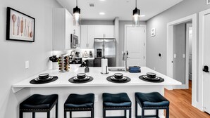 A modern kitchen with white cabinetry, a stainless steel refrigerator, and a central island with bar stools. - Charming 1-bedroom apartment in Fort Worth with WiFi, AC, fitness room (Fort Worth)