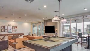 A modern living room with a pool table, comfortable seating, a large TV, and a city view. - Charming 1-bedroom apartment in Fort Worth with WiFi, AC, fitness room (Fort Worth)