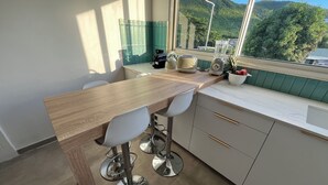 A modern kitchen with a wooden countertop, two white chairs, and a view of a mountain landscape through the window. - Modern apartment in beachfront residence - hill view (Grand-Case)