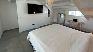 A bedroom with a bed, a TV, a desk with a laptop, a mirror, and a chandelier. - Modern apartment in beachfront residence - hill view (Grand-Case)
