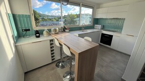 A modern kitchen with a large island, bar stools, a sink, and a view of a scenic landscape. - Modern apartment in beachfront residence - hill view (Grand-Case)