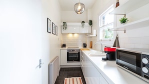 Una cucina moderna con mobili bianchi, forno integrato, microonde e finestra sopra il lavello.