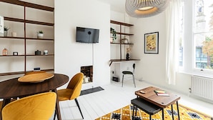 Un soggiorno moderno con un tavolo da pranzo in legno, sedie gialle, una TV montata a parete e un'ampia finestra con vista sugli edifici.