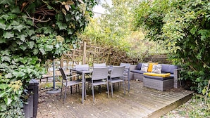 Patio esterno con mobili in vimini, un molo in legno e vegetazione circostante.