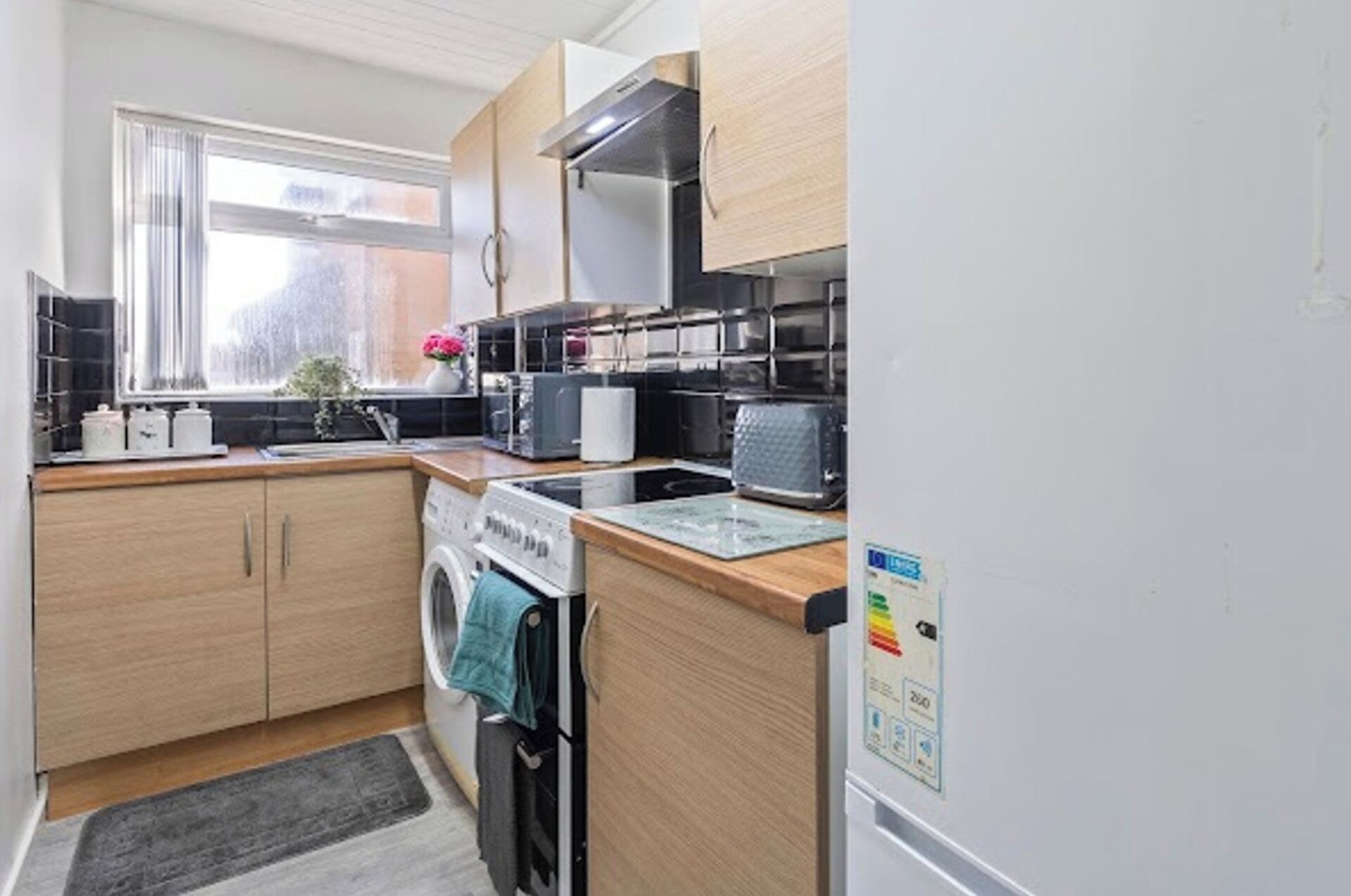 A compact kitchen with wooden cabinets, a built-in oven, a microwave, and a washing machine.