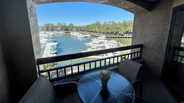 A balcony with a view of a marina, a round table with a vase, and two chairs. - Gorgeous 2 bedroom villa overlooking Shelter Cove Harbour with pool and spa (Hilton Head Island)