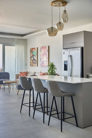 A modern kitchen with a central island, bar stools, a refrigerator, and pendant lighting.