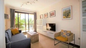 Een woonkamer met een bank, een televisie, een stoel en een groot raam.