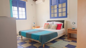 Ein Zimmer mit Bett, Nachttisch, kleinem Tisch und Fenster mit blauen Fensterläden.