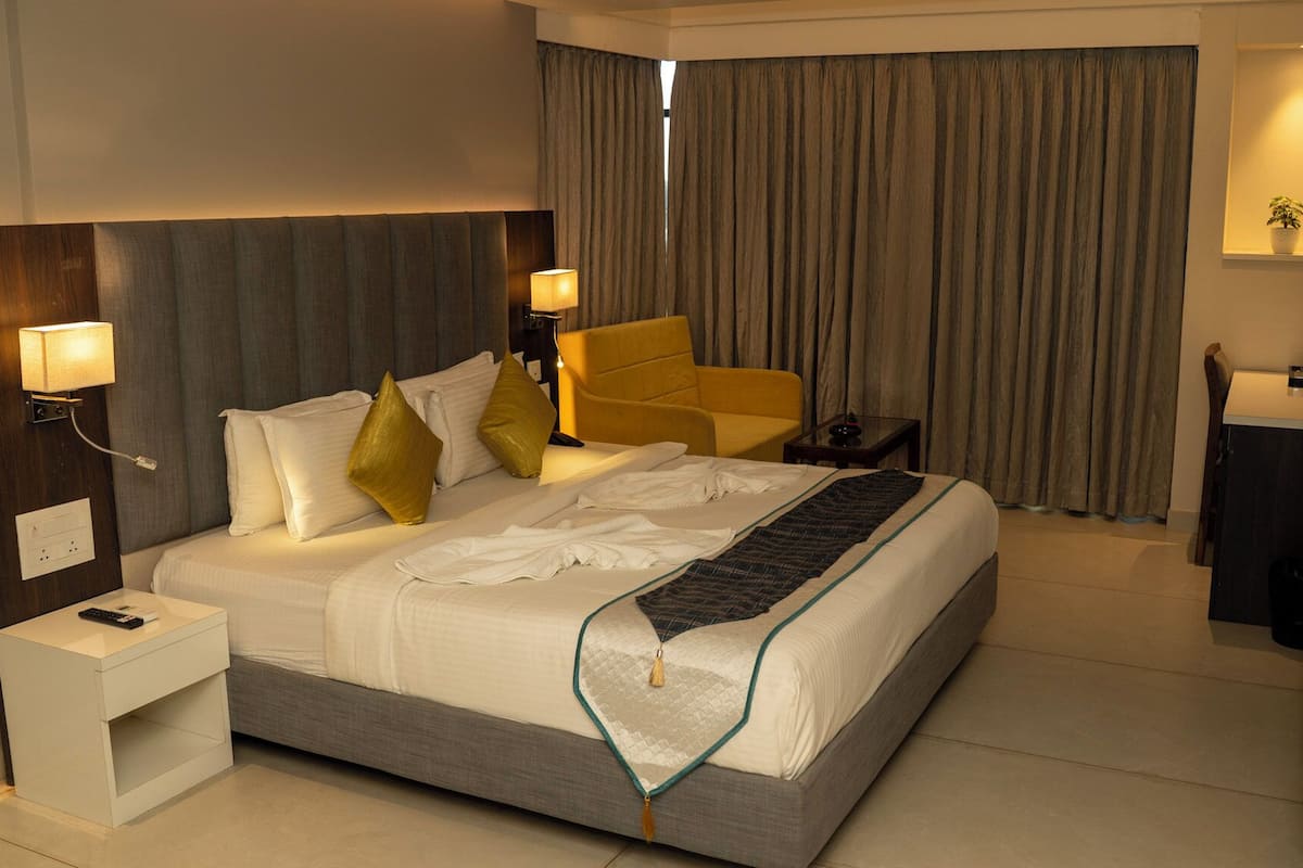 A hotel room with a large bed, two bedside lamps, a nightstand, a chair, a desk, a mirror, and a window with curtains.