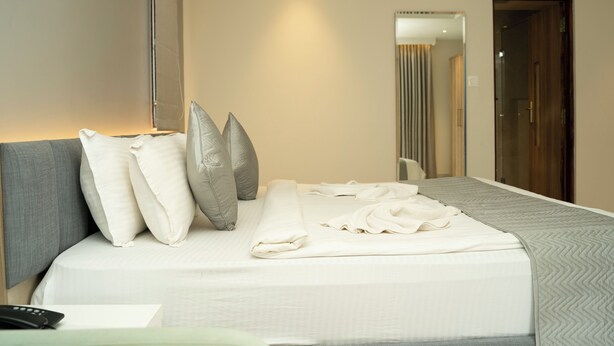 A neatly made bed with pillows, a remote control, and a folded towel on a hotel room bed.