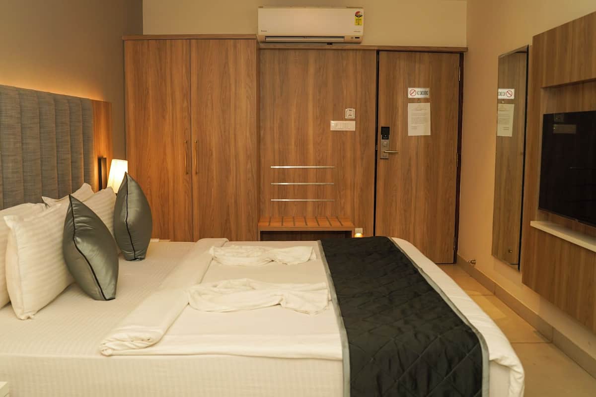 A hotel room with a bed, a wardrobe, a television, and an air conditioning unit.