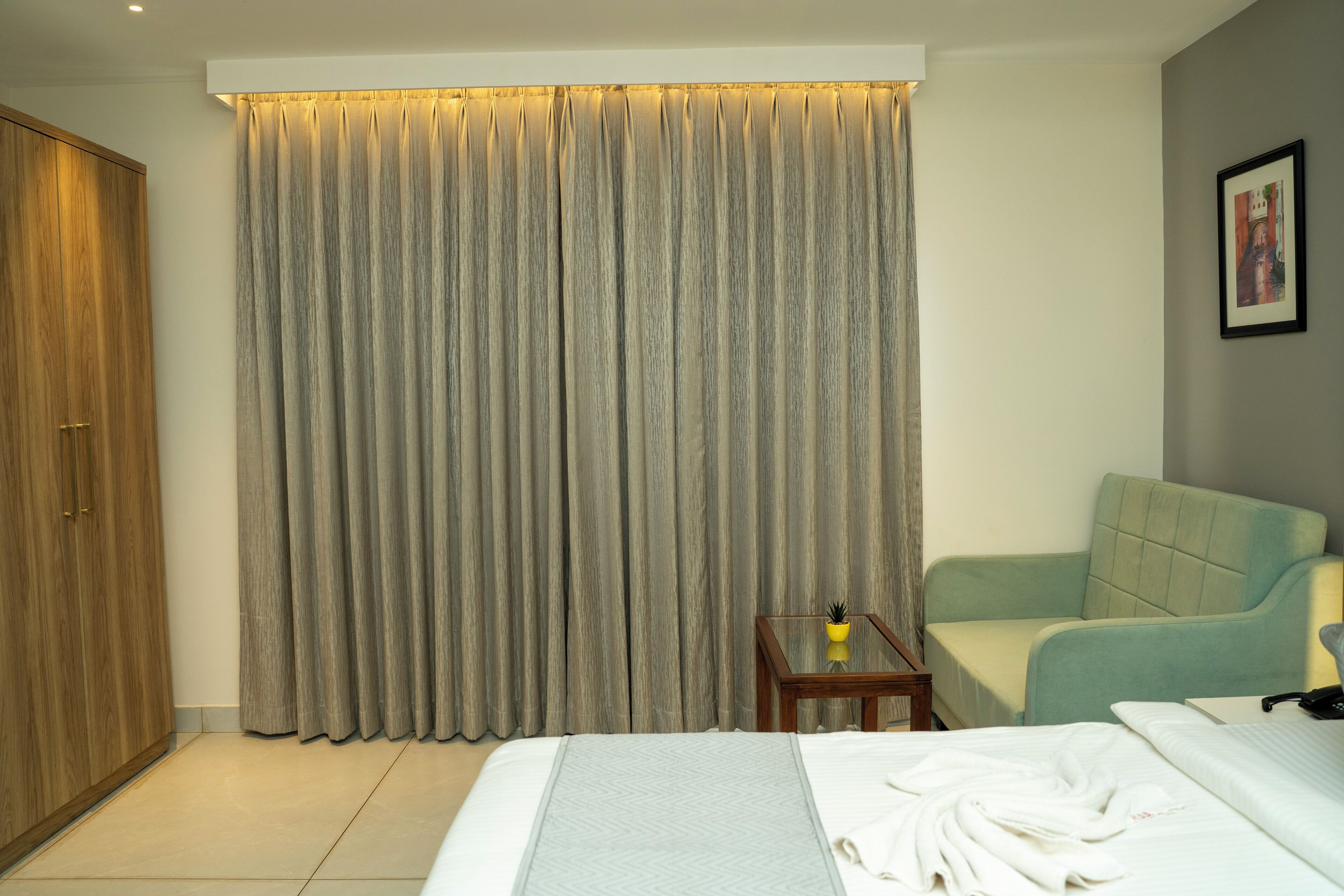 A hotel room with a bed, a seating area, a wardrobe, and a curtain.
