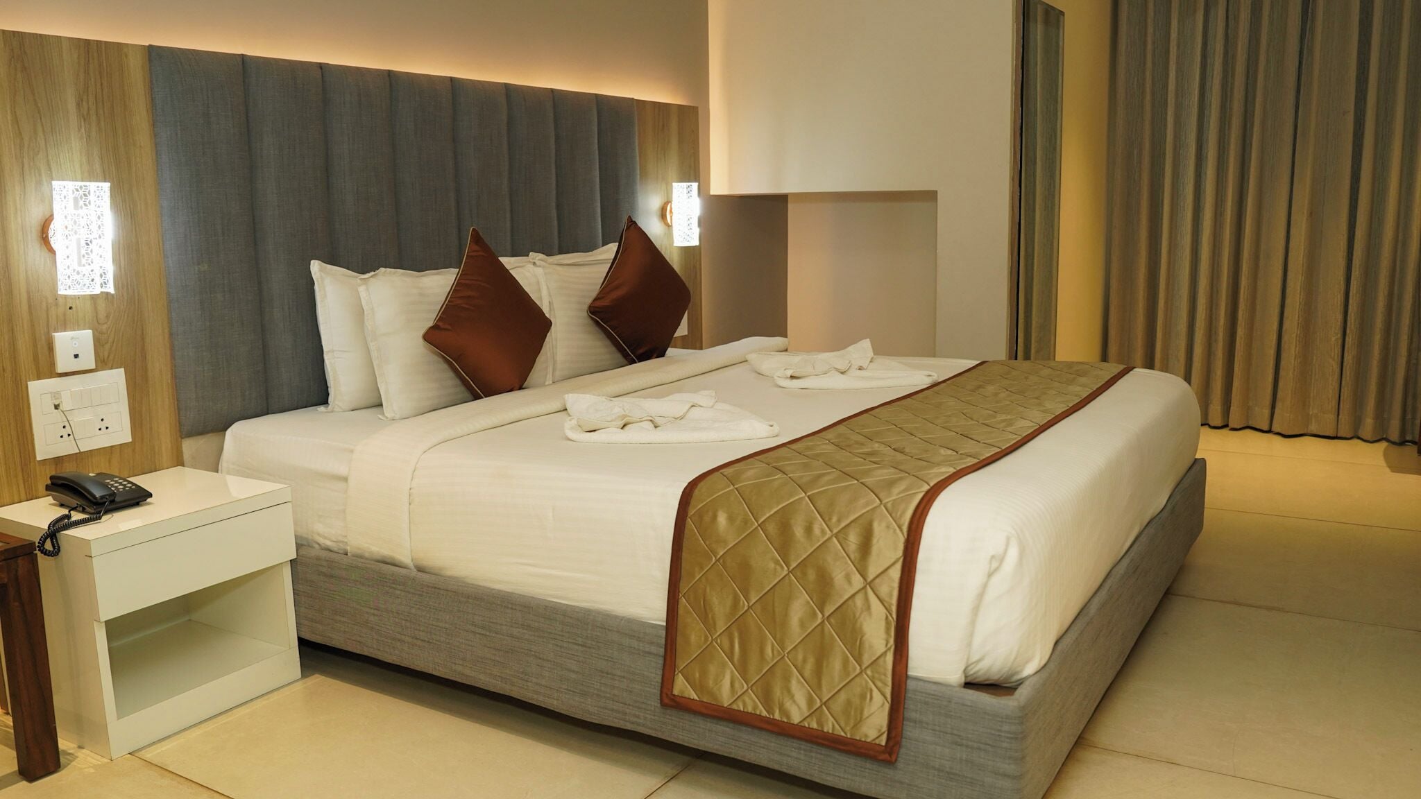 A hotel room with a large bed, a bedside table with a phone, and a wall-mounted light.
