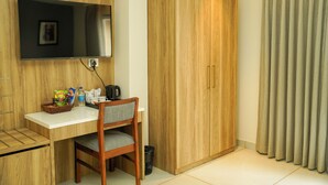 A hotel room with a wooden desk, a television mounted on the wall, a wardrobe, and a curtain.