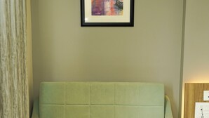 A green sofa with a glass coffee table in front, a framed picture on the wall, and a lamp on a side table.