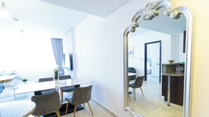 Een moderne eetruimte met een marmeren tafel, grijs gestoffeerde stoelen en een grote, versierde spiegel die de ruimte weerspiegelt.