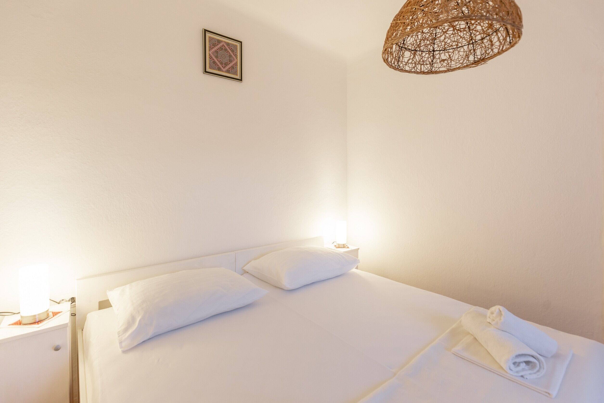 Un letto rifatto con lenzuola bianche, un asciugamano bianco e un lampadario intrecciato sopra.