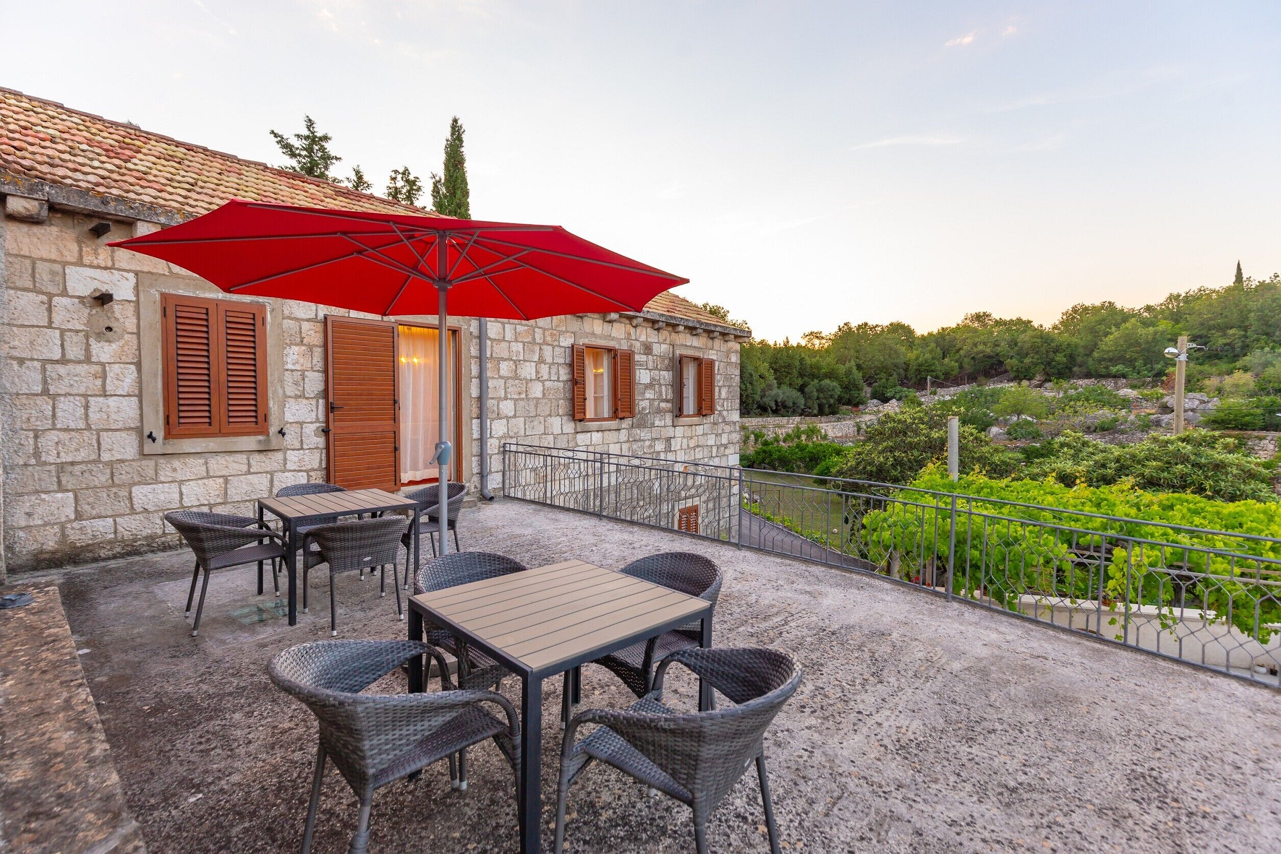 A stone building with a terrace, outdoor seating, and a red umbrella.