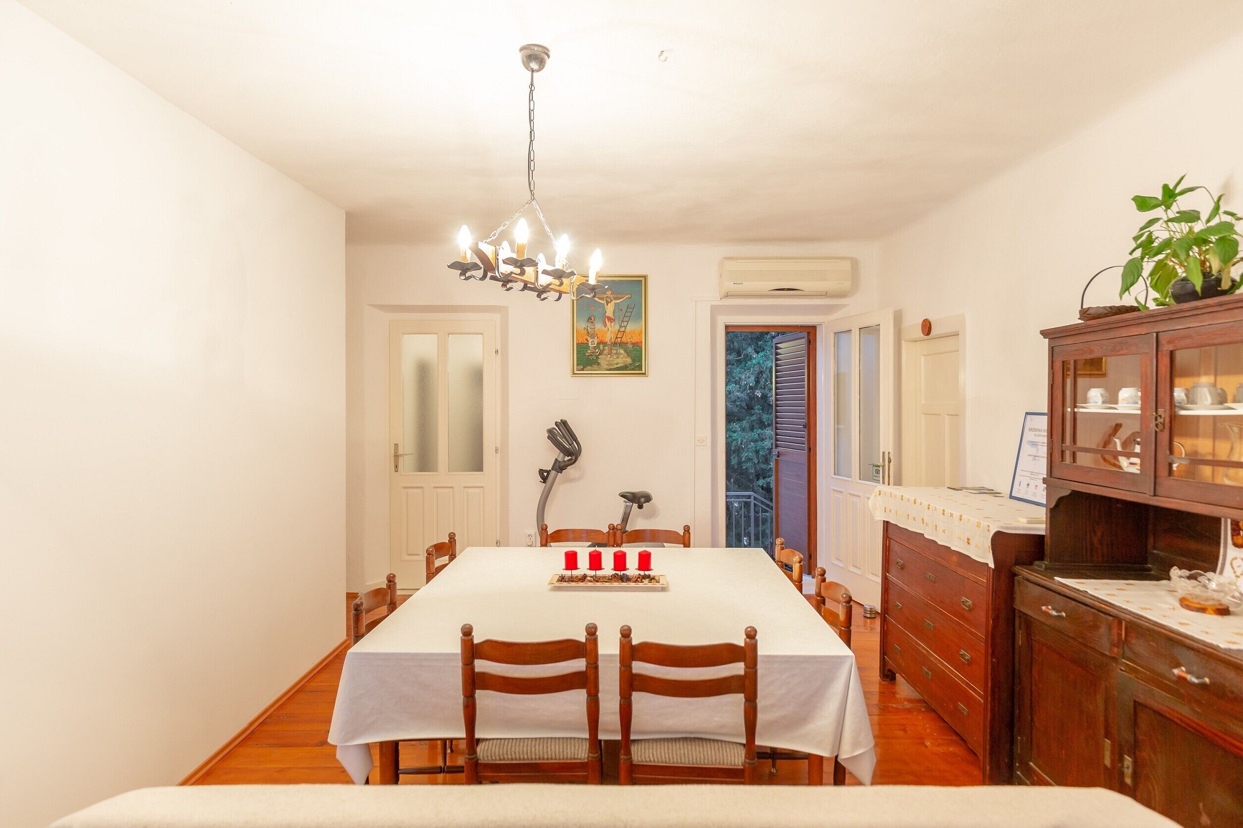 A dining room with a white table, wooden chairs, a chandelier, and a cabinet with glass doors.