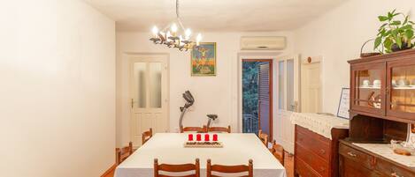 A dining room with a white table, wooden chairs, a chandelier, and a cabinet with glass doors.
