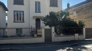 A two-story building with a symmetrical facade, a central entrance, and a small garden area with a metal fence.